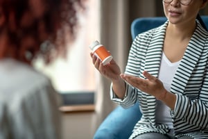 person presenting a pill bottle to a client